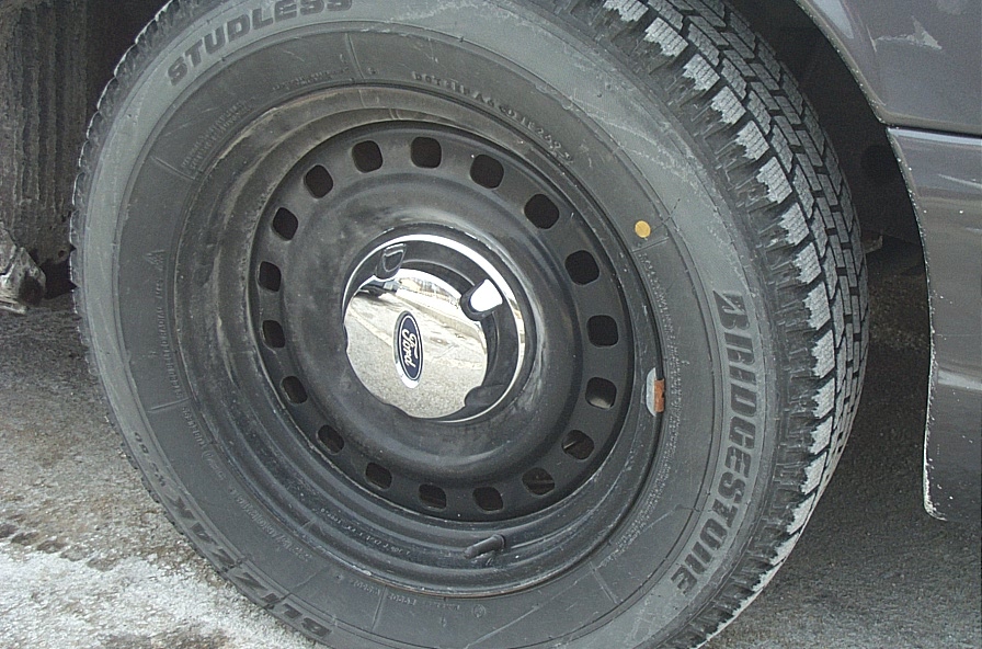 Close-up of a black steel wheel with a chrome Ford hubcap on a Bridgestone tire