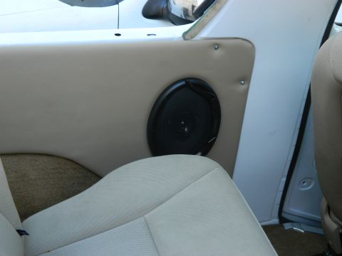 1979 Ford Bronco - The interior of a vehicle shows a tan door panel with an aftermarket speaker. The seat fabric is visible in the foreground.