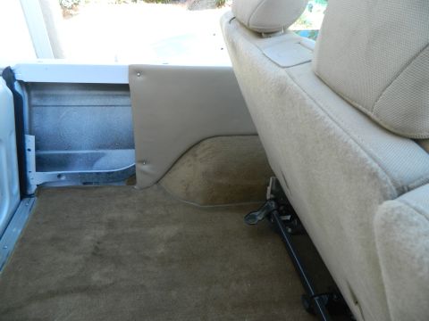 1979 Ford Bronco - The interior of a vehicle shows tan carpeting and beige upholstery, with a visible seat adjustment mechanism.