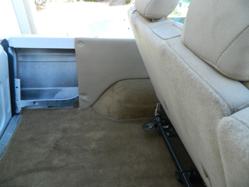 Car interior with tan carpet and beige seats, showing the rear cargo area and a seat adjustment lever