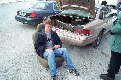 1991 Ford LTD Crown Victoria - Man sits on a car seat next to a 1991 Ford Crown Victoria LTD with its trunk open; another similar car is behind.