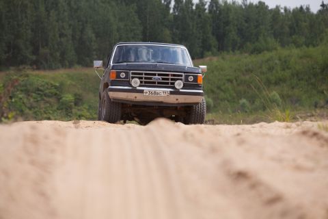 1987 Ford Bronco - 1987 Ford Bronco driving on a dirt road with trees in the background.