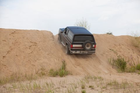 1987 Ford Bronco - A black 1987 Ford Bronco navigates a sandy incline, kicking up dust.