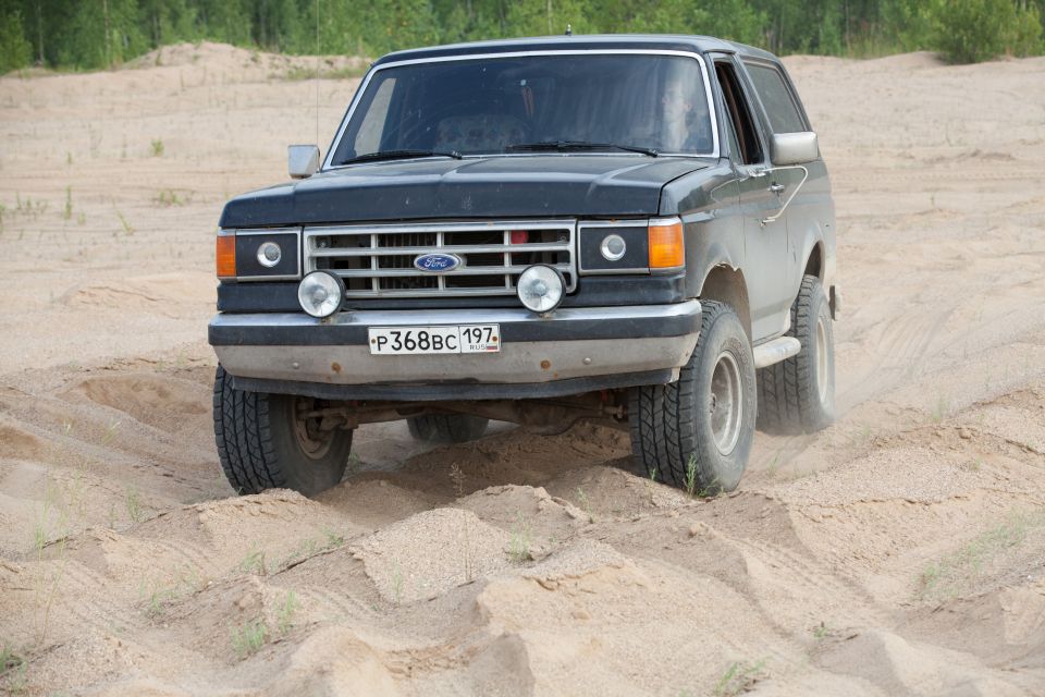 Black 1987 Ford Bronco driving on sand, front 3/4 view