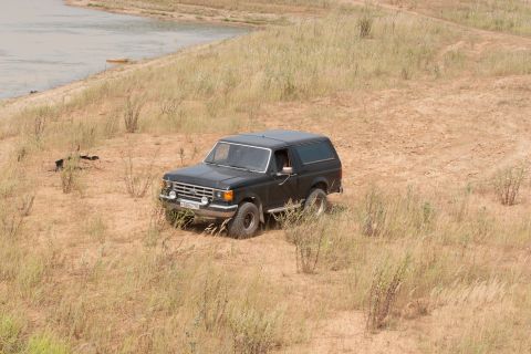 1987 Ford Bronco - Black 1987 Ford Bronco sits on a dry, grassy embankment next to a calm body of water.