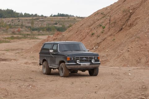 1987 Ford Bronco - A black Ford Bronco is parked on a dirt road with a large sandy hill in the background.