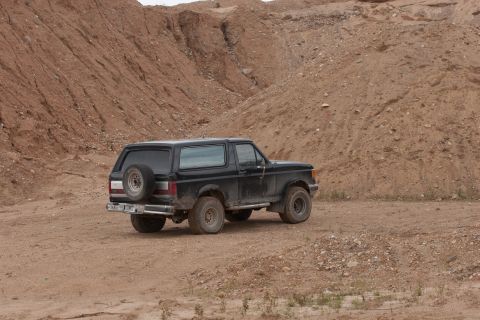 1987 Ford Bronco - A black 1987 Ford Bronco is seen from a three-quarter front view in a sandy, off-road environment.