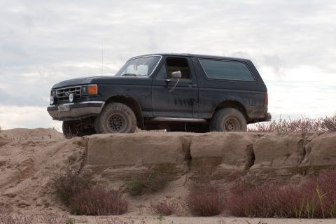 1987 Ford Bronco - 1987 Ford Bronco on a dirt mound under a cloudy sky.