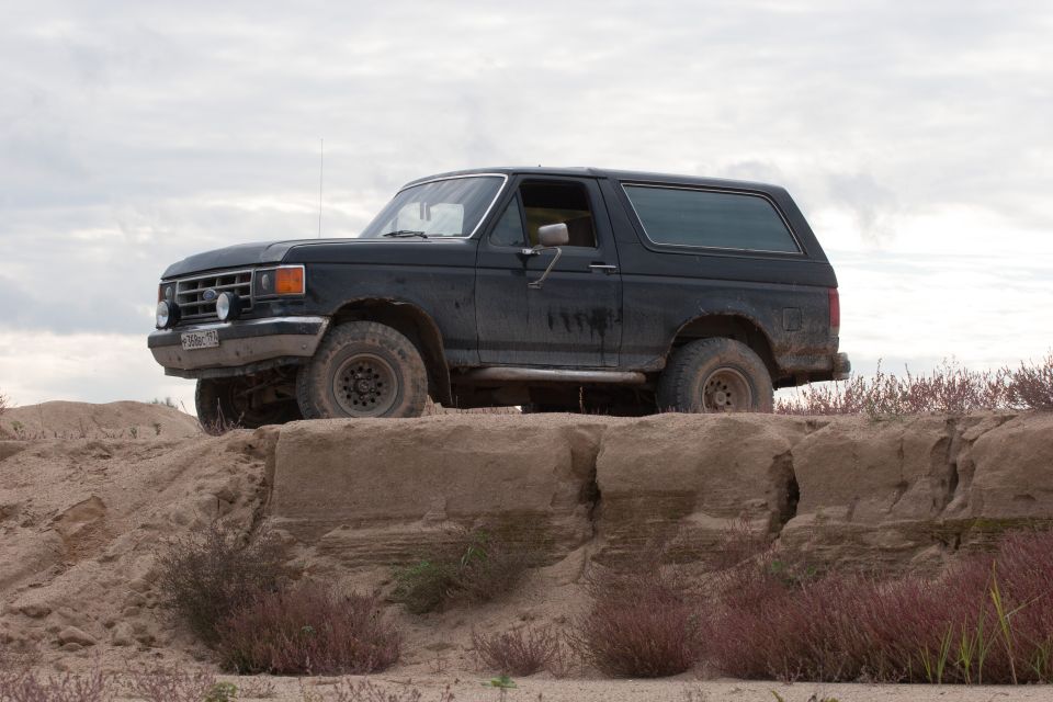 1987 Ford Bronco parked on a dirt embankment with scrub brush around