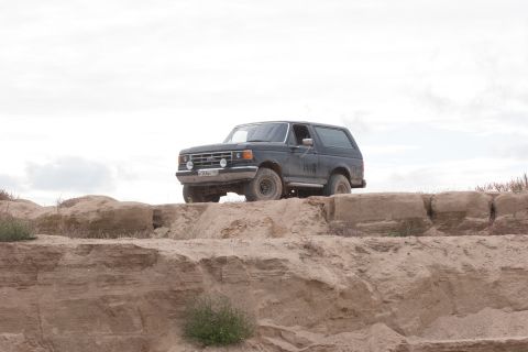 1987 Ford Bronco - A Ford Bronco is positioned on a sandy ridge against a cloudy sky.