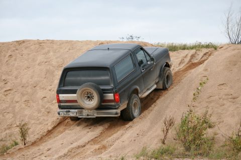 1987 Ford Bronco - Black 1987 Ford Bronco navigates a sandy incline, showing its rear and spare tire.
