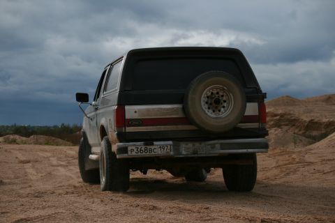 1987 Ford Bronco - The rear of a 1987 Ford Bronco is shown on a dirt road under a cloudy sky.