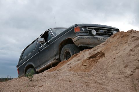 1987 Ford Bronco - Ford Bronco navigates a sandy incline under an overcast sky.