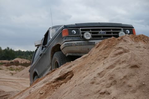 1987 Ford Bronco - This 1987 Ford Bronco is navigating a steep sand dune in an outdoor, dusty environment.
