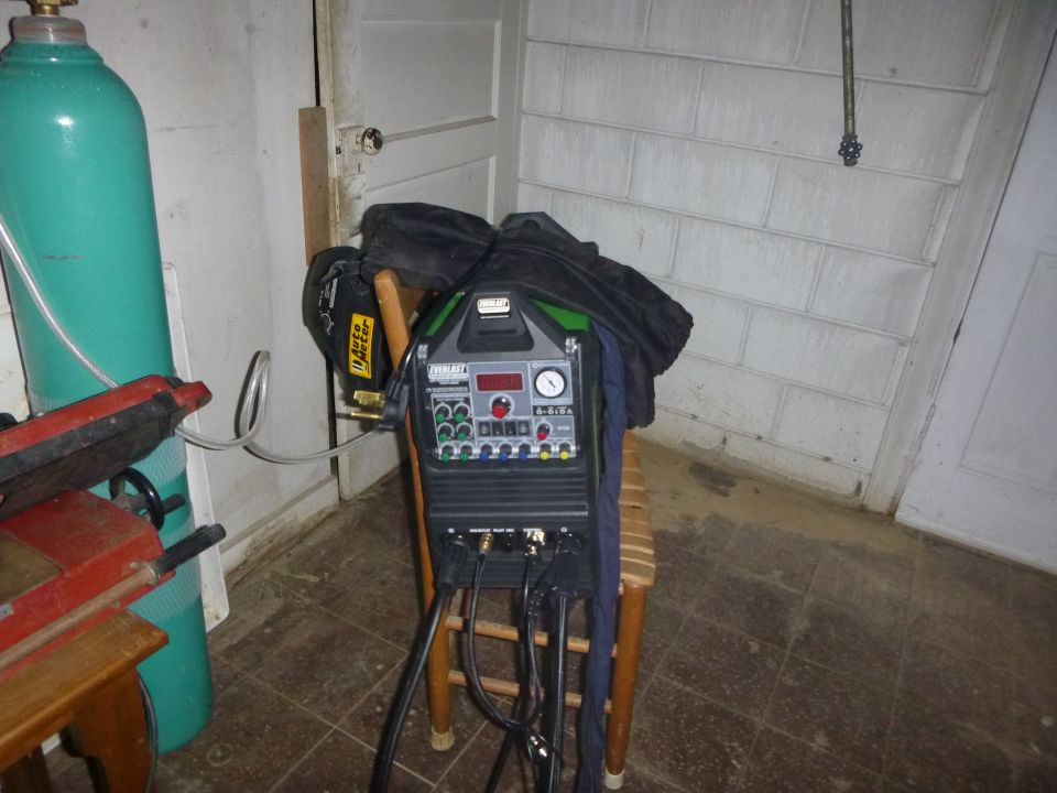 Welding machine on a chair next to a green gas cylinder and a red tool