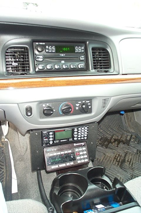 1991 Ford LTD Crown Victoria - The interior of a car shows a dashboard with a radio, climate controls, and two mounted two-way radios.