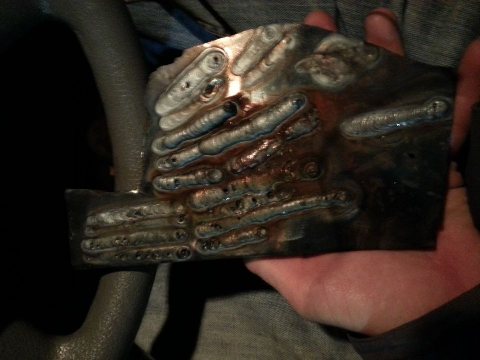 Someone's holding a metal plate with lots of welds on it. Part of a steering wheel is visible
