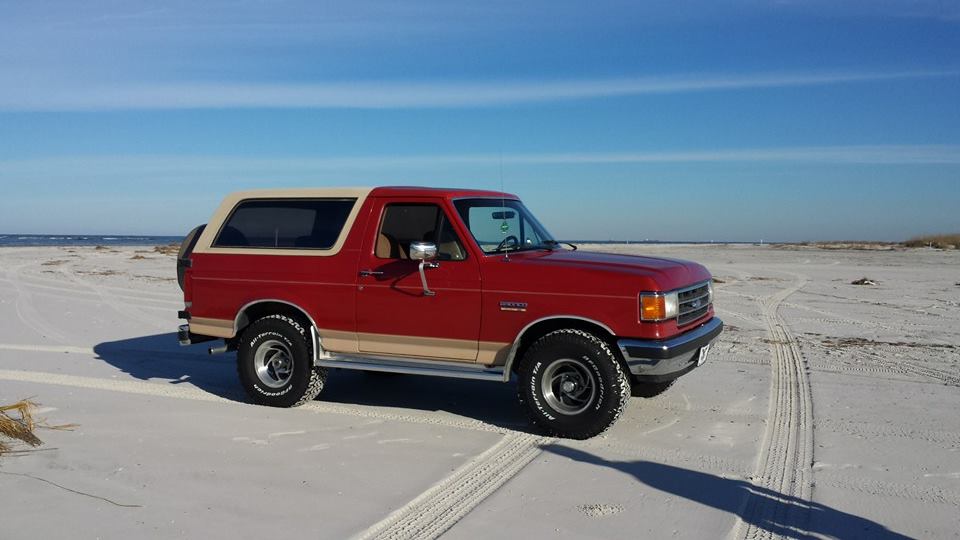 1991 Ford Bronco parked on a beach with tire tracks in the sand