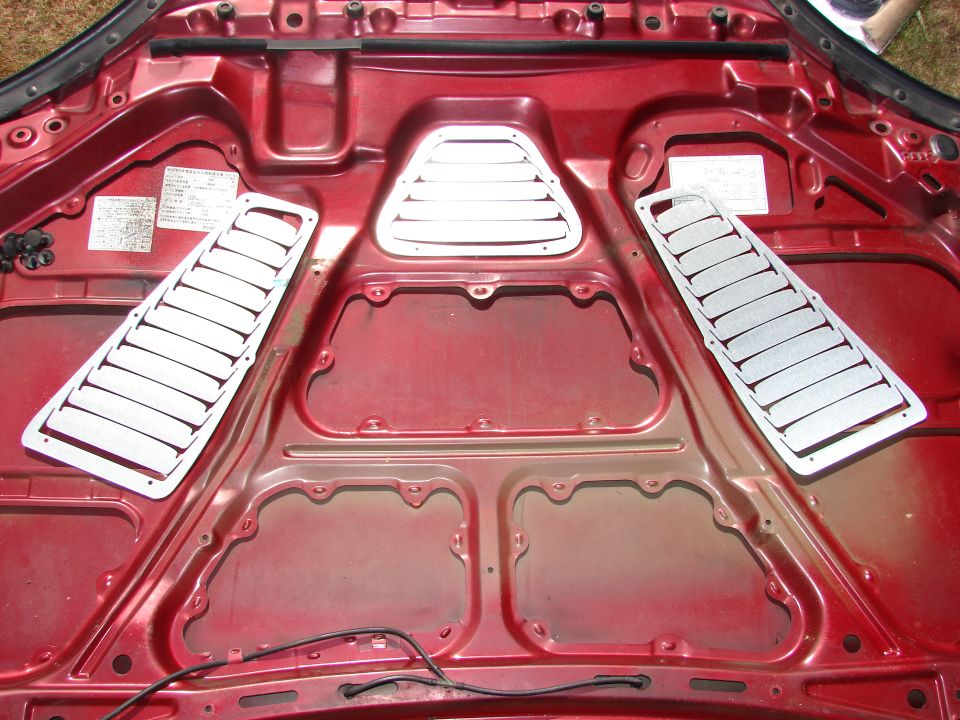 Red car hood interior with two rectangular and one triangular silver vent covers installed