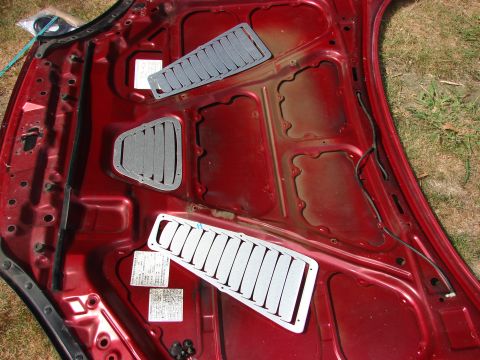 1993 Mazda MX-3 - Underside of a red car hood with vent inserts and stickers, possibly for a Mazda MX-3.