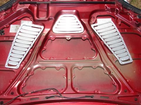 1993 Mazda MX-3 - Underside of a red car hood with aftermarket louvered vents installed.