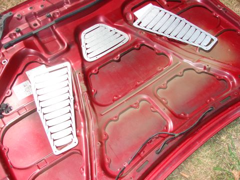 1993 Mazda MX-3 - Aftermarket hood vents installed on the underside of a red car hood.