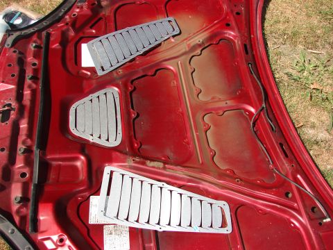 1993 Mazda MX-3 - Aftermarket louvered vents are placed on the underside of a red car hood.