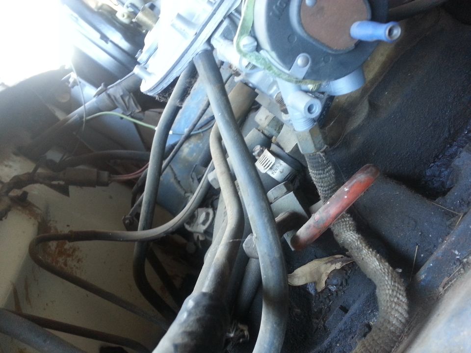 Engine bay close-up showing carburetor, fuel lines, and various hoses. Some rust is visible