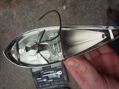 1978 Ford Bronco - A person holds a chrome tail light assembly, showing its internal components and a 'TAIWAN' stamp, with a toolbox in the background.