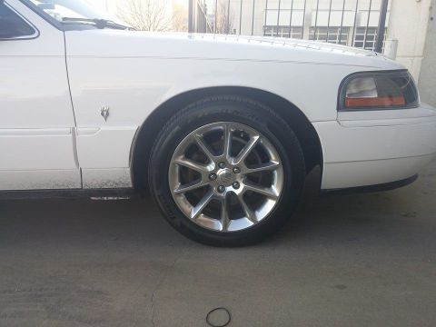 2000 Mercury Grand Marquis - A close-up view of the front passenger side of a white Mercury Grand Marquis, highlighting the wheel and fender area.