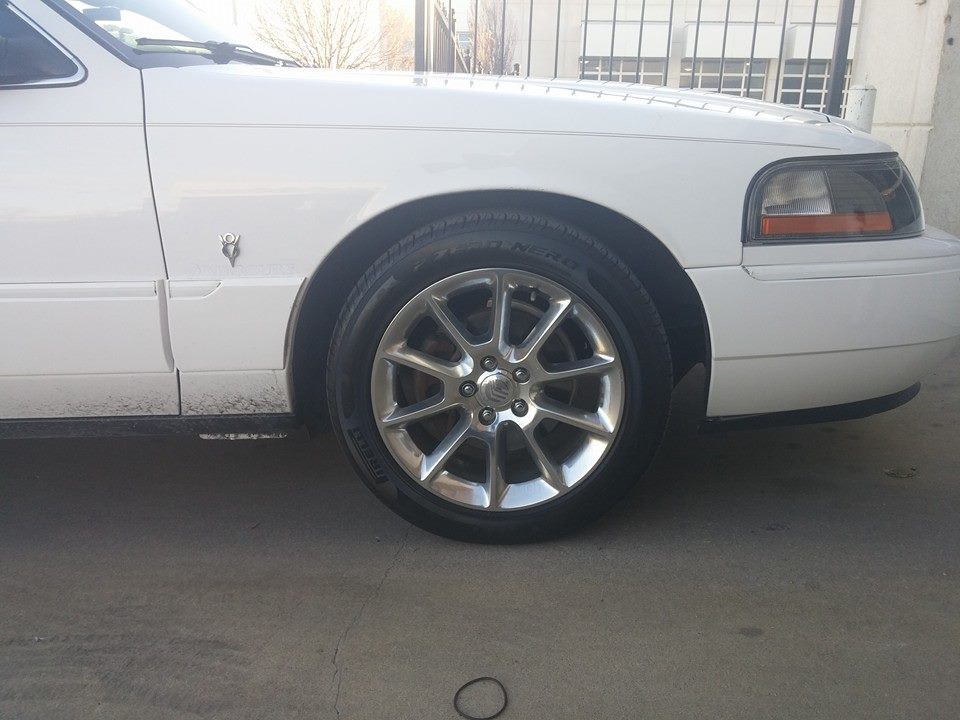White Mercury Grand Marquis front fender and wheel. Has chrome rims and a Mercury emblem on the fender