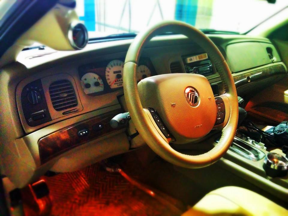 Tan dashboard and steering wheel of a 2000 Mercury Grand Marquis, with wood trim and a central Mercury logo on the airbag