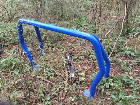 1971 Ford F-250 - A blue roll cage rests on the forest floor amidst foliage and fallen branches.