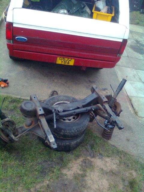 1989 Ford Bronco - Disassembled rear axle and suspension components are visible on the ground near a Ford pickup truck.