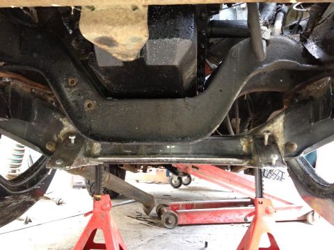 1989 Ford Bronco - Undercarriage view of a vehicle supported by jack stands, revealing suspension components and the engine oil pan.