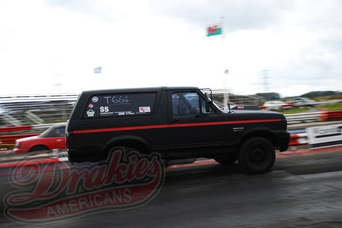 Black Ford Bronco with red stripe and "T664 SS" sticker on window, driving on a track
