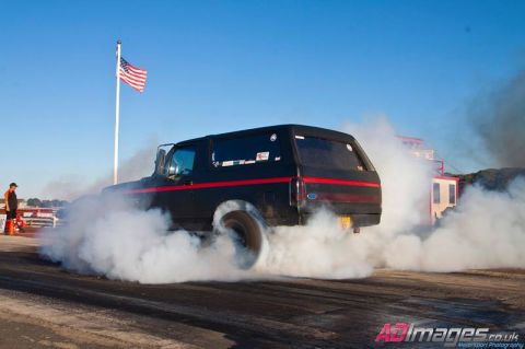 1989 Ford Bronco - A black Ford Bronco with red racing stripes performs a burnout, kicking up a large cloud of smoke.