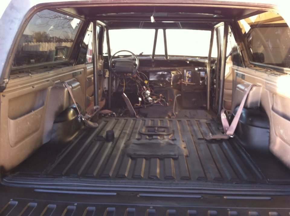 Interior of a vehicle with seats removed, roll cage installed, and dashboard wiring exposed