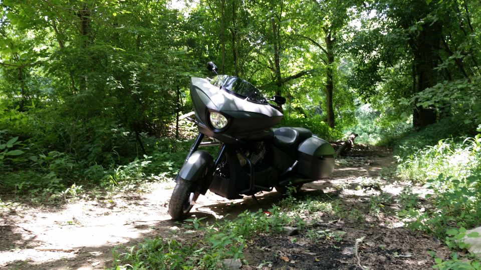 Black motorcycle parked on a dirt path in a wooded area