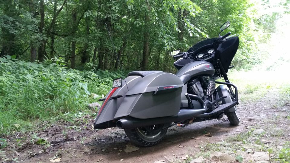 Gray motorcycle with saddlebags parked on a dirt path in a wooded area