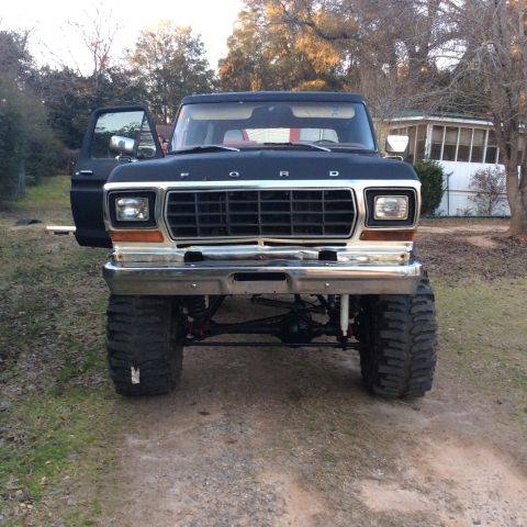 1979 Ford Bronco - This lifted Ford truck features a prominent grille and chrome bumper, with the driver's side door ajar.
