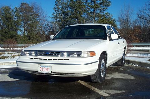 1991 Ford LTD Crown Victoria - A white Ford Crown Victoria police car is parked in a lot on a sunny day with some snow on the ground.