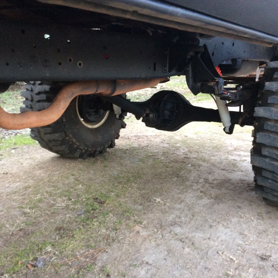 Undercarriage of a lifted vehicle showing a large tire, exhaust pipe, and rear axle