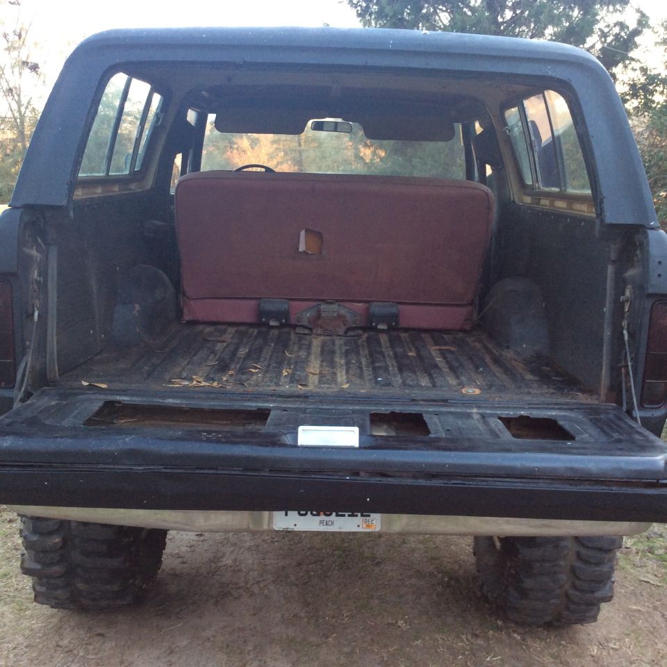 Rear view of a dark blue 1978 Ford Bronco with a maroon bench seat and a dirty cargo bed