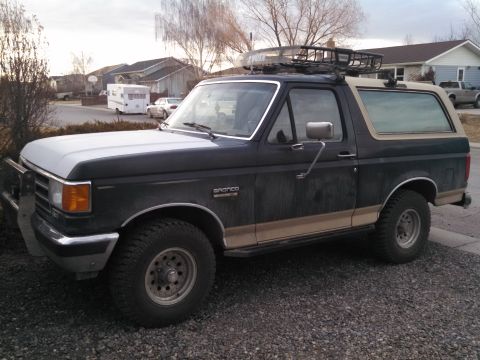 1991 Ford Bronco - A Ford Bronco with a roof rack and brush guard is parked on a gravel driveway.