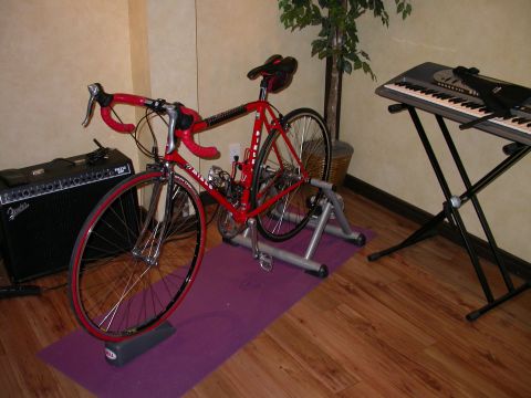 1968 Chevrolet Camaro - A red road bicycle is set up on a trainer, ready for indoor use, next to musical equipment.