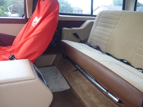 1985 Ford Bronco - The interior of a vehicle shows tan seats and a red car cover on the driver's side.