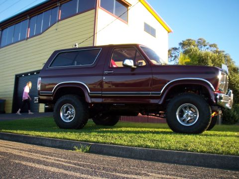 1985 Ford Bronco - Maroon 1985 Ford Bronco parked on grass with a yellow building in the background.