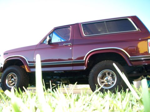 1985 Ford Bronco - Maroon 1985 Ford Bronco parked in grass, viewed from the side.