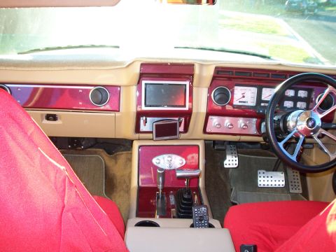 1985 Ford Bronco - The custom interior features red upholstery, a prominent aftermarket steering wheel, and a central console with a digital screen and shifte…